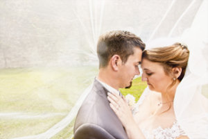 Bei einer Hochzeit in Heidersbach lehnen umarmen sich Braut und Bräutigam unter ihrem Brautschleier.
