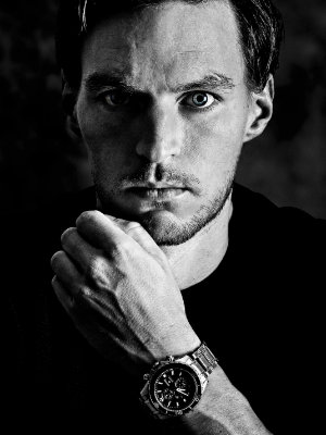 Schwarz-weißes, kontrastreiches Portraits eines Mannes mit bläulichen Augen.