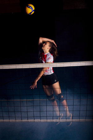Volleyballerin mit angewinkeltem Angriffschlag hinter Netz, während am Boden Nebel zu sehen ist.