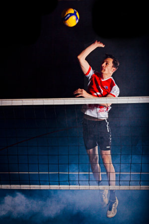 Volleyballerin mit angewinkeltem Angriffschlag hinter Netz, während am Boden Nebel zu sehen ist.